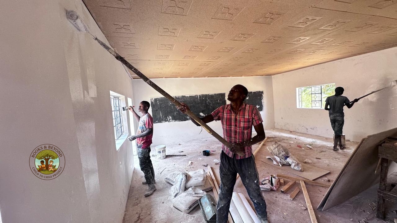 The work begins. Three painters roll fresh white onto the library walls while ceiling boards go up overhead. What was a bare shell is becoming something new.