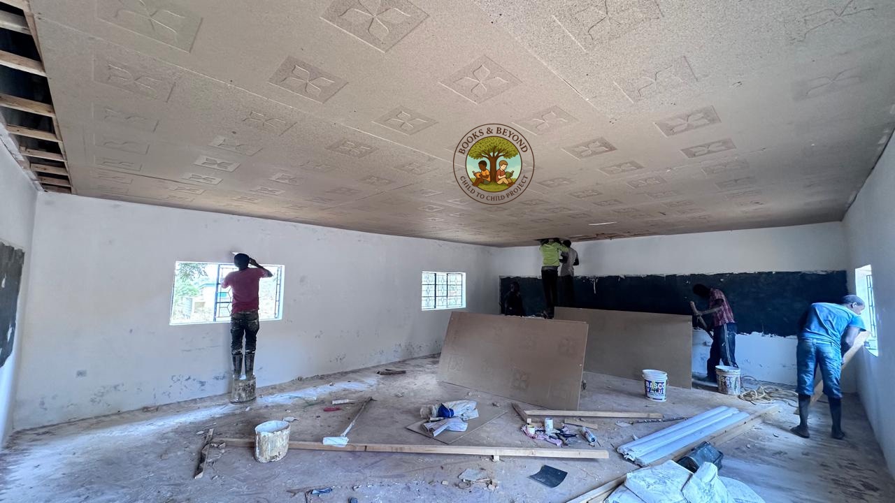 The interior renovation in full swing — walls being whitewashed, the lower blackboard border taking shape, and a team of four working together to turn an empty room into a library. This is what transformation looks like from the inside.